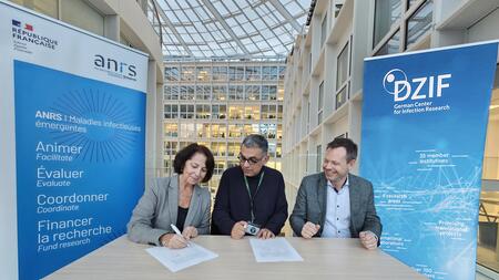 DZIF Executive Board member Prof. Maura Dandri, DZIF managing director Dr Timo Jäger and ANRS | MIE Director Prof. Yazdan Yazdanpanah at the signing ceremony of the MoU at ANRS | MIE in Paris. Standing in the background are Roll-ups of ANRS | MIE and DZIF.