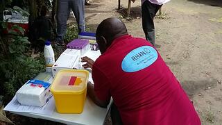 A member of the RHINO team leans over a table with laboratory and test materials set up in a village in Tanzania.