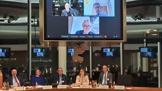 Mitglieder des PKAMR in einem Sitzungssaal, andere Personen sind über einen großen Monitor zugeschaltet