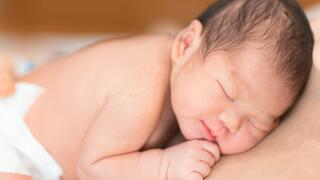 Newborn baby wearing only a diaper lying face-down on the skin of a person