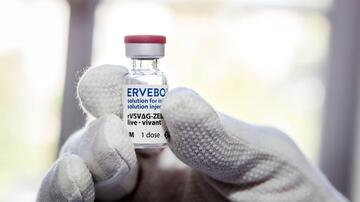 A gloved hand holds a vaccine vial labeled “Ervebo_solution for injection_rVSVΔG-ZEBOV-GP_live_1 dose”