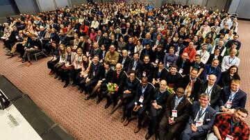 Photo of a large crowd of people in a lecture hall, taken from a bird's eye view.