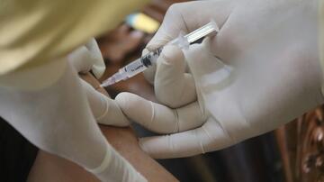 A close-up image of a healthcare professional wearing white gloves administering a vaccine injection into a person's upper arm using a syringe.