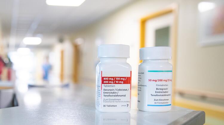 Zwei Behälter mit antiretroviralen Kombinationspräparaten mit den Bezeichnungen „Darunavir/Cobicistat/Emtricitabine/Tenofoviralafenamide” und „Bictegravir/Emtricitabine/Tenofoviralafenamide” stehen auf einer Ablage in einem hellen Krankenhausflur.