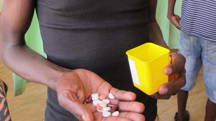 Teilansicht eines dunkelhäutigen Mannes, der verschiedenfarbige Pillen auf der Handfläche seiner rechten Hand hält und in der linken Hand eine gelbe Plastikdose 